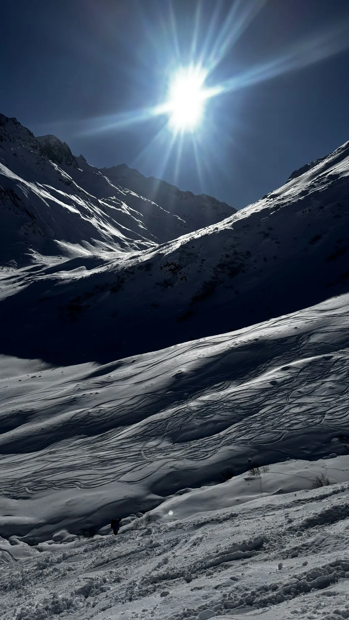 Ski tracks across a sunlit slope with the sun above the ridge