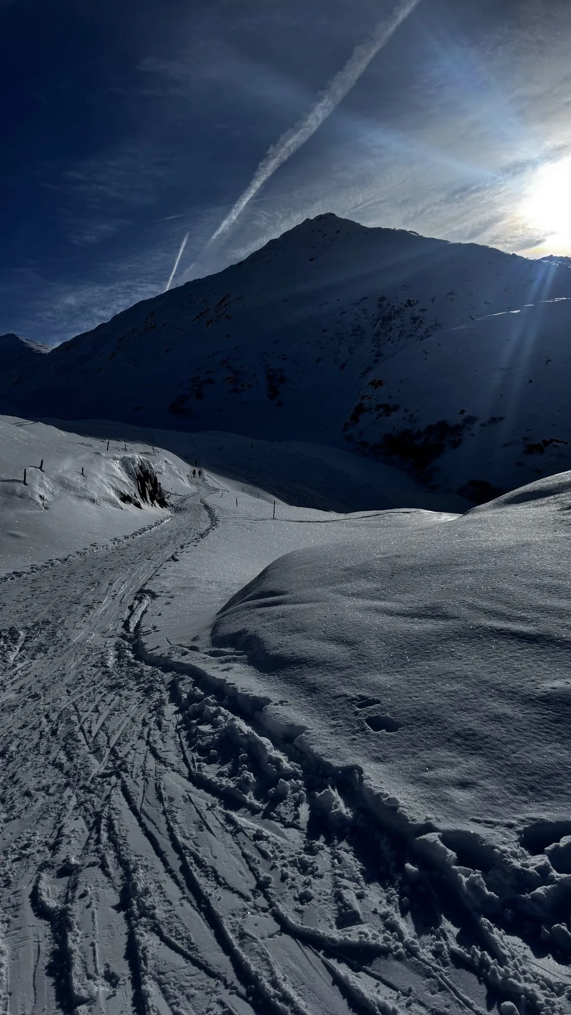 Ski tracks in the snow leading towards a peak, with the sun behind it